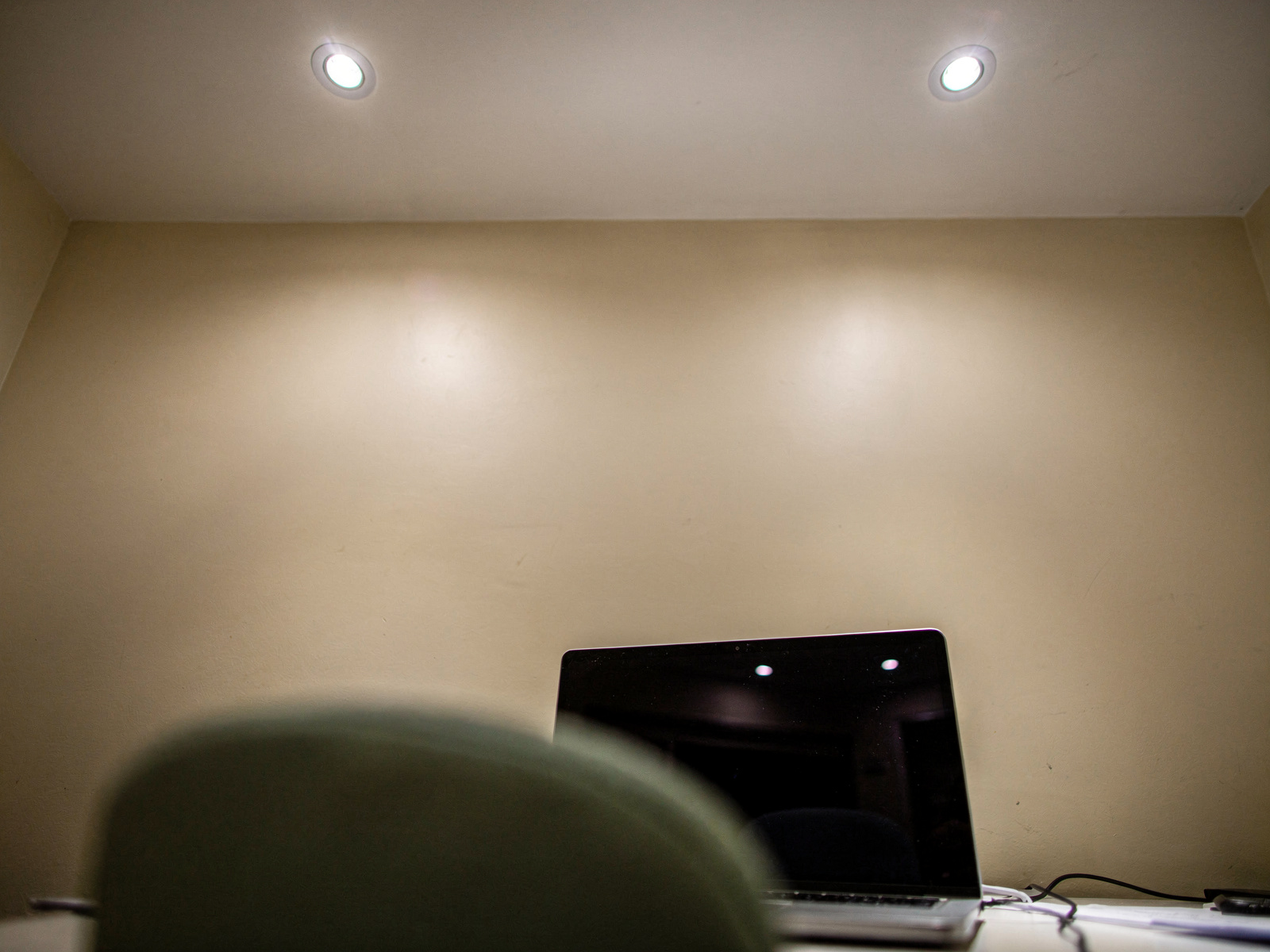 A small home office ceiling with recessed halogen spotlights switched on, casting hard pools of light onto a desk below.