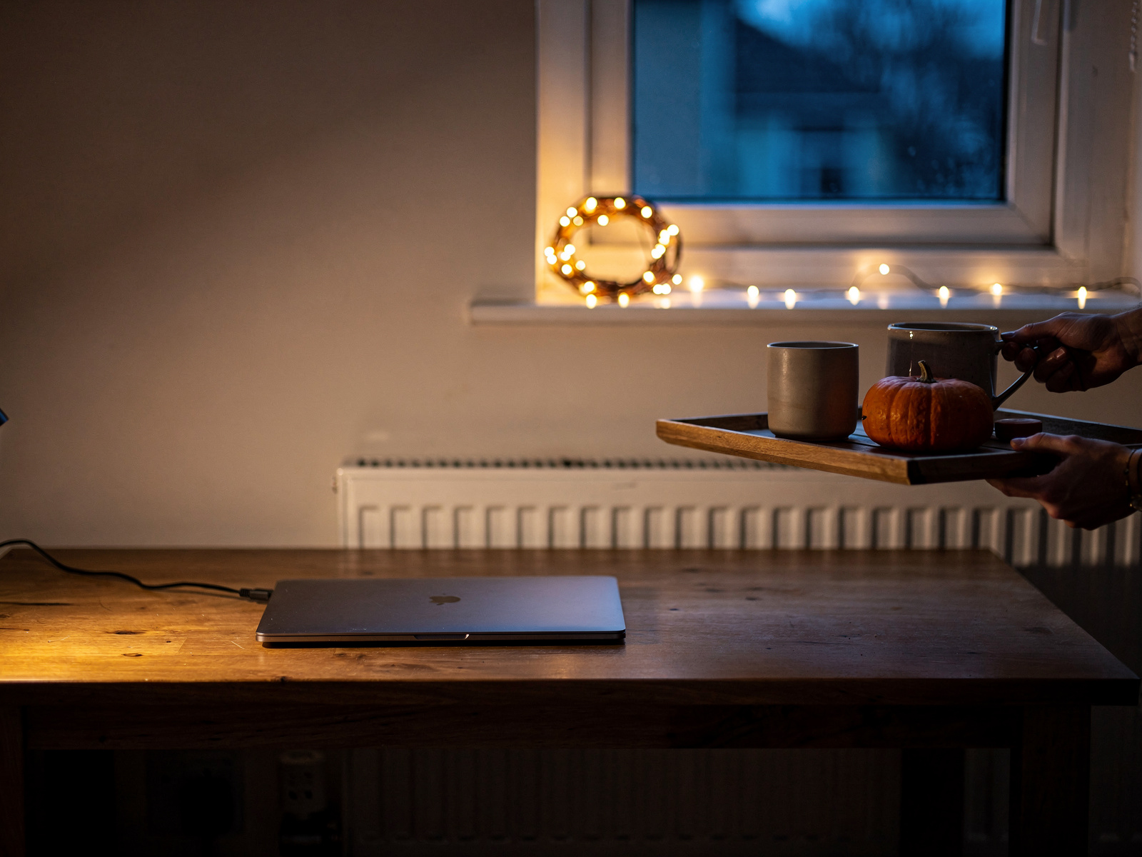 A cleared home desk at dusk with a closed laptop, the fairy lights unplugged and a tray with a mug and mini pumpkin being carried away.