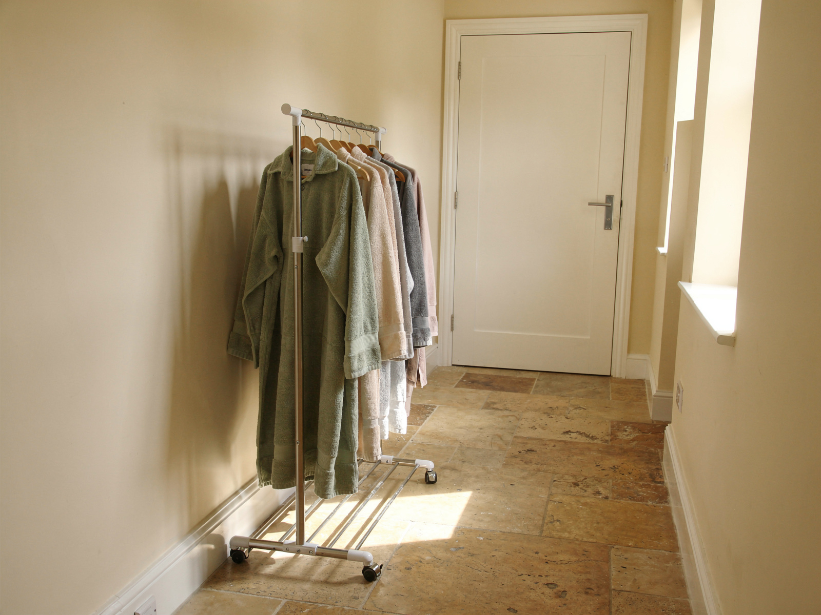 A clothes airer loaded with towels in a hallway, with the door to a small home office closed behind it, in plain daylight.