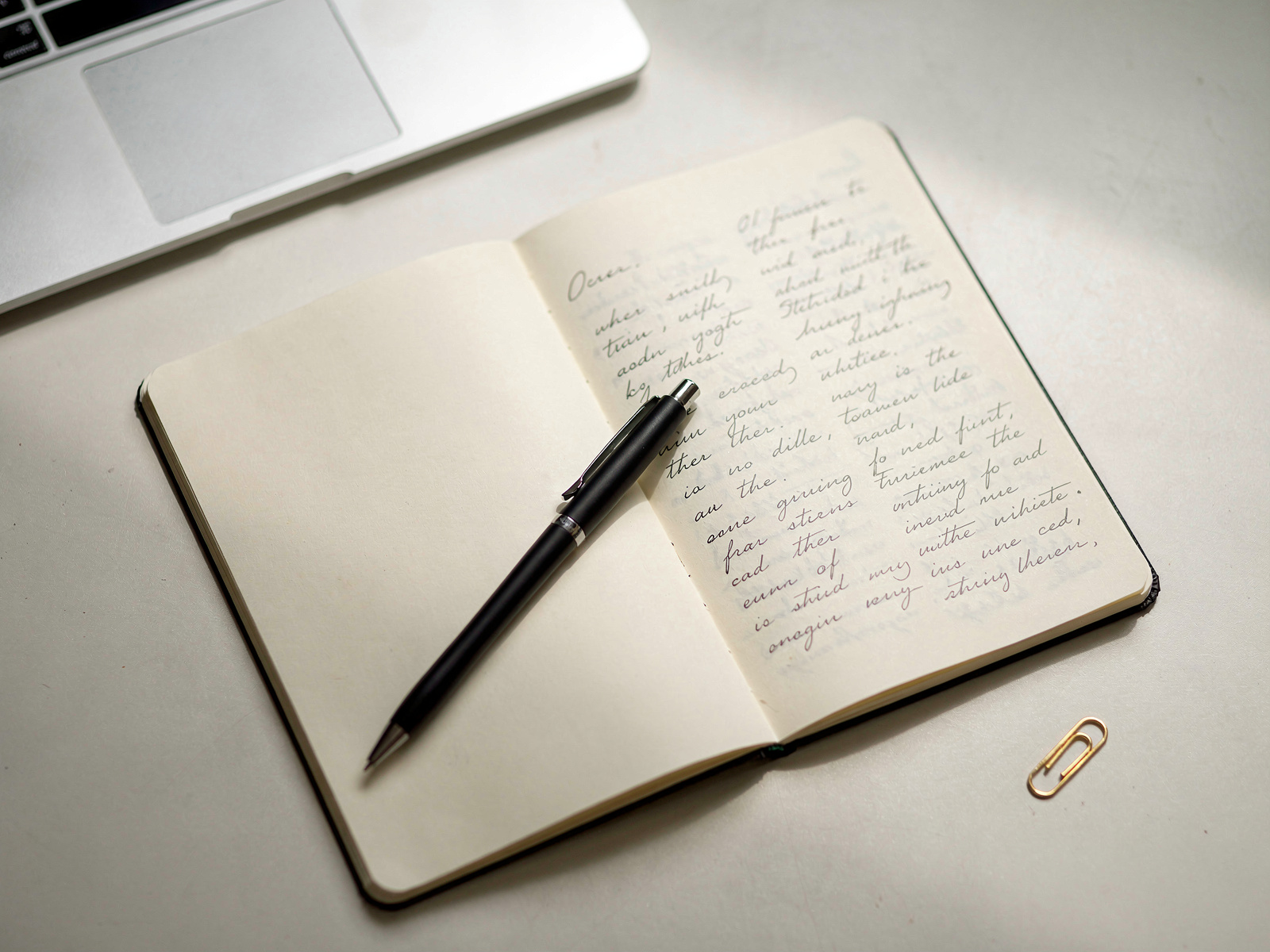 A notebook open on a desk with two short handwritten lists side by side and a pen resting across the page, in soft daylight.