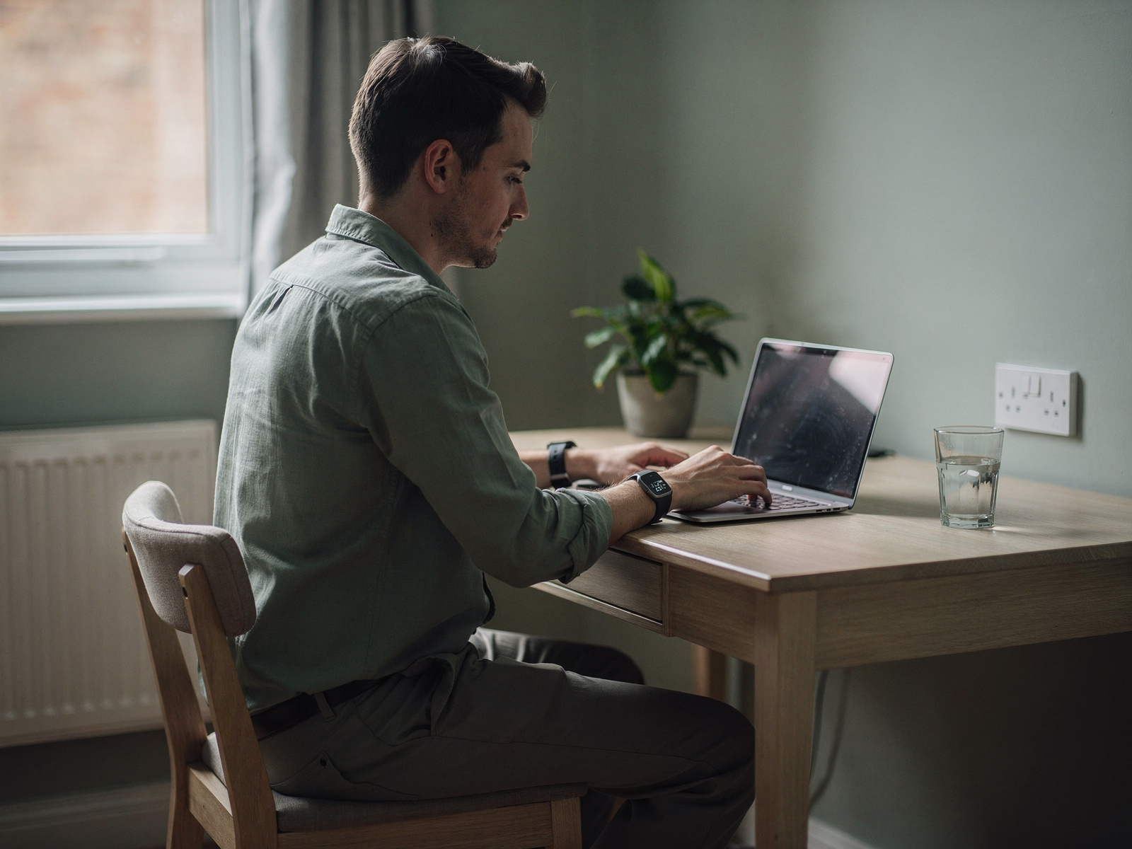 A home worker at a tidy desk wearing a slim screenless band while typing on a laptop, soft window light.