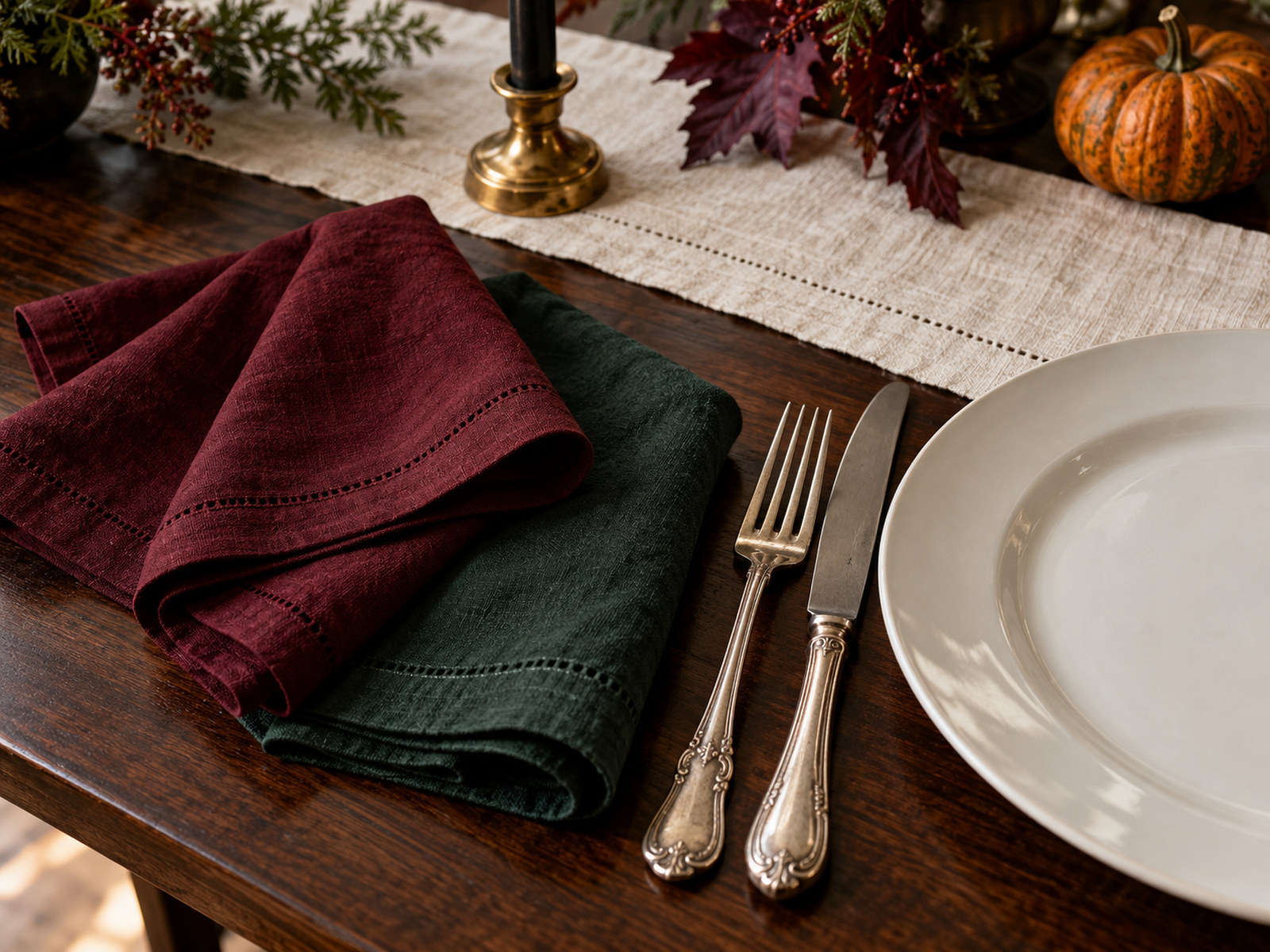 Burgundy and forest-green napkins with a white plate and silver cutlery on dark wood