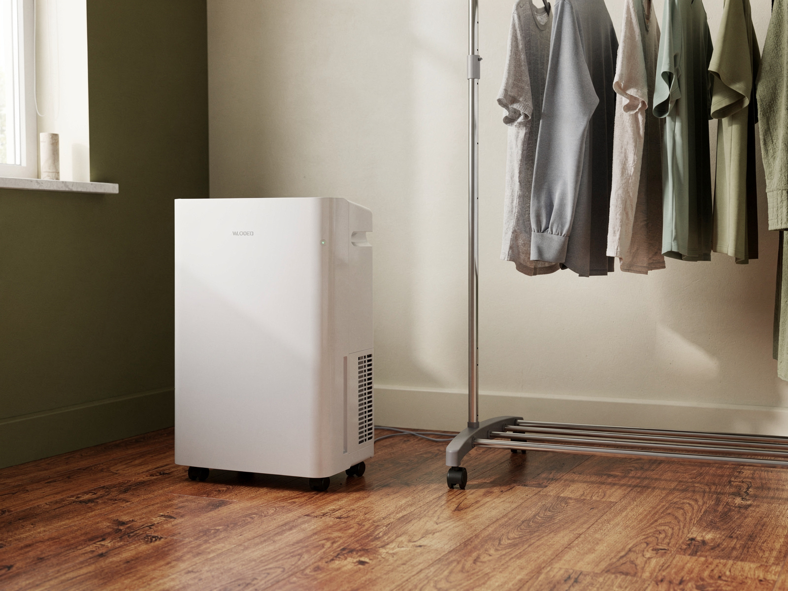 A compact dehumidifier standing on a hard floor in a small spare room beside a clothes airer, daylight coming through a window.
