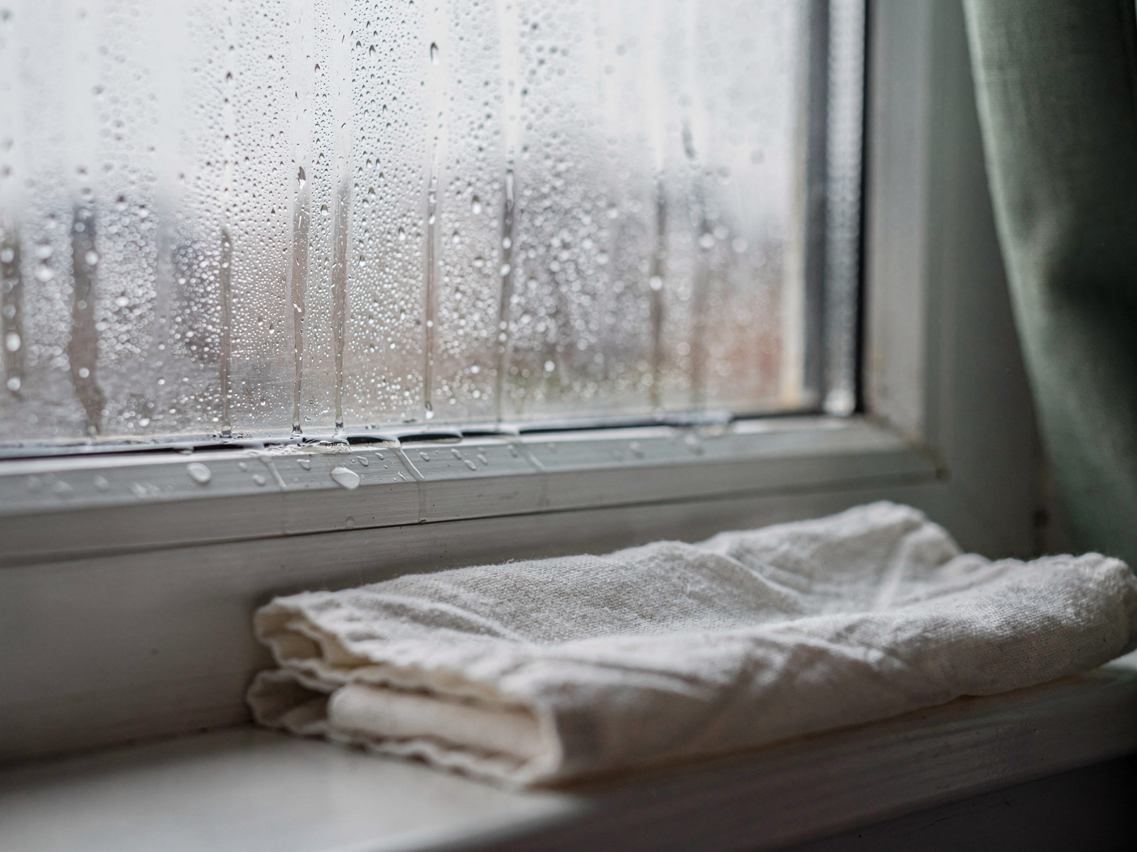 Morning light on a bedroom window with beads of condensation on the glass and a folded cloth on the sill.