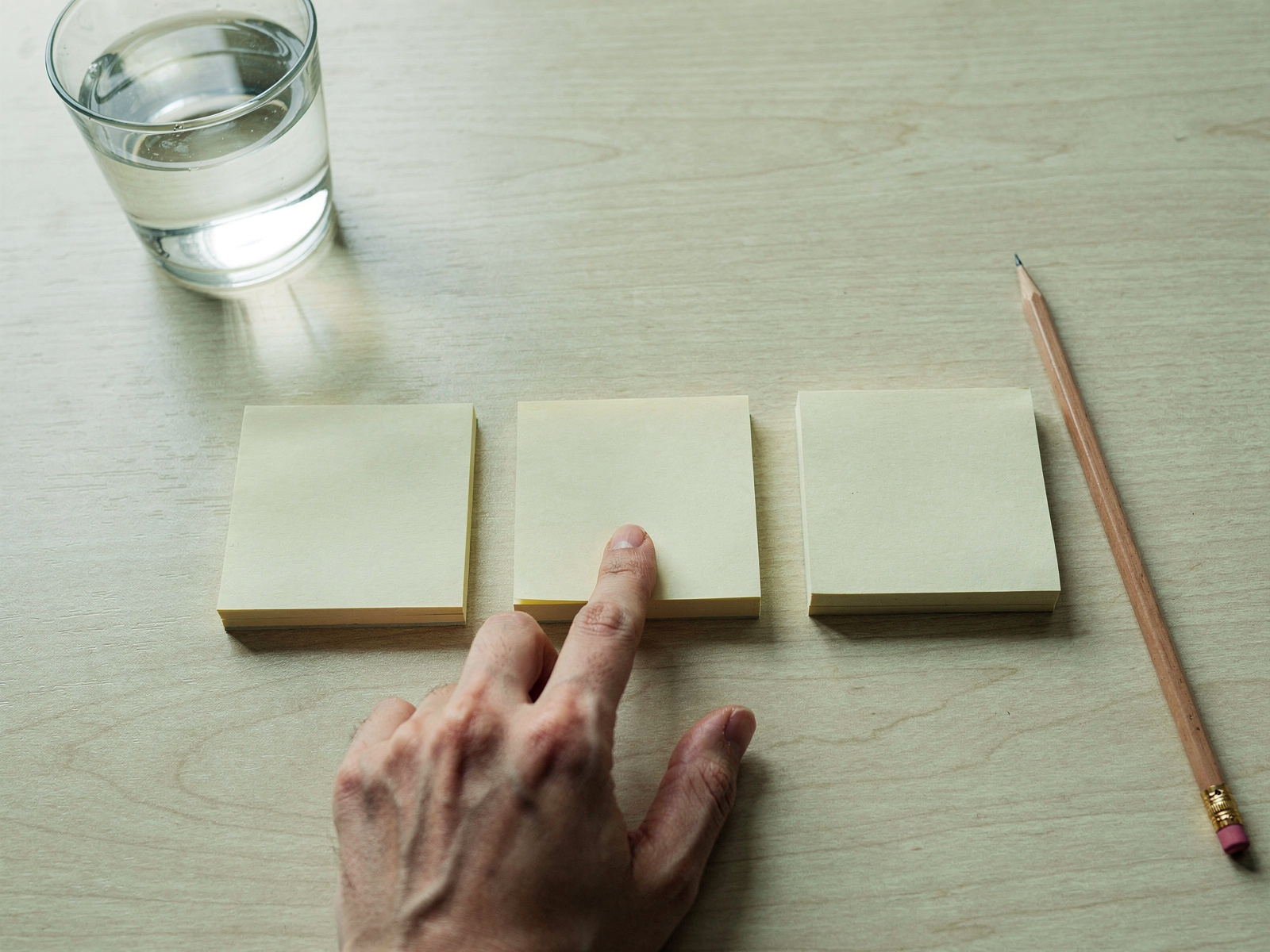 Three small piles of sticky notes on a wooden desk, sorted beside a laptop, with a hand placing one note on the middle pile.